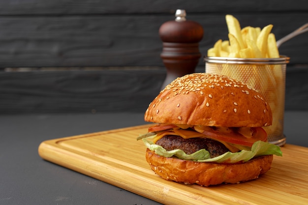 Delicious burger and fries on wooden board against black surface