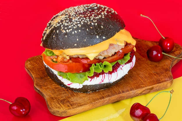 Delizioso hamburger da un panino nero con una cotoletta su una tavola con pomodori e formaggio cetriolo e lattuga su fondo rosso fast food