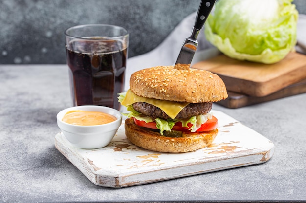 Delicious burger pierced with knife with sauce and cola