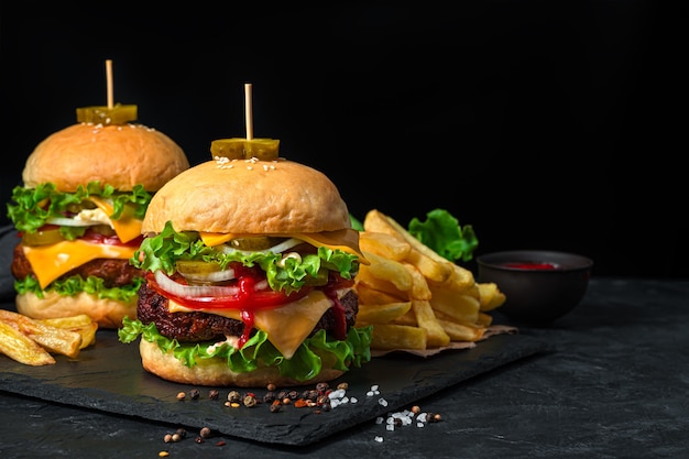 フライドポテトと黒の背景に牛肉、野菜、チーズのおいしいハンバーガー。側面図、コピースペース。