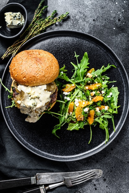 Delicious Burgers with blue cheese, bacon, marbled beef and onion marmalade, a side dish of salad with arugula and oranges. Black background. Top view