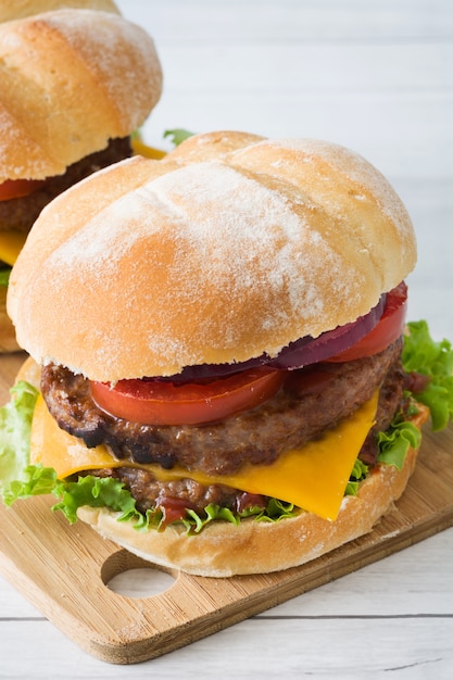 Delicious burgers with cheddar cheese, tomato, lettuce and onion  on white wooden table