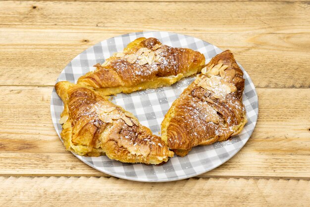 Deliziosi croissant al burro con fette di sciroppo di mandorle e zucchero a velo sul tavolo di legno grezzo