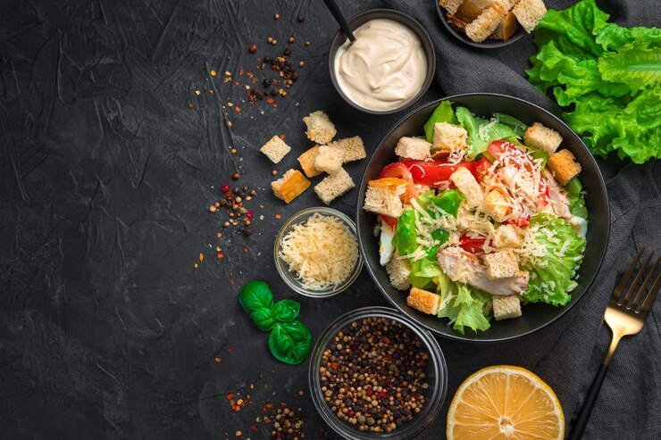Фотография вкусный салат цезарь с ингредиентами, лимоном и специями на черном фоне. вид сверху с копией пространства.