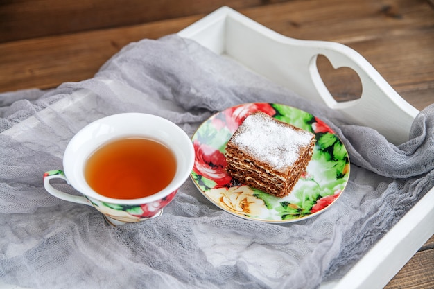 Delicious cake and a cup of hot tea on a white tray.