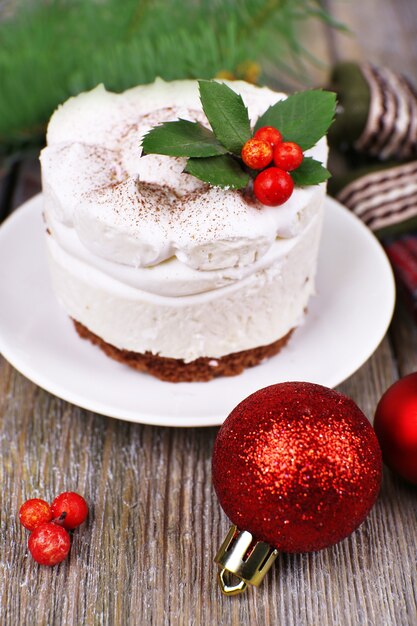Фото Вкусный торт на блюдце с падубом и ягодами на новогоднем украшении и деревянной поверхности