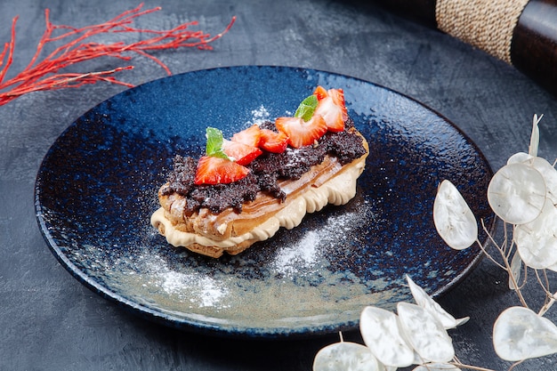 Delicious cake Profiteroles with truffle paste, custard and strawberries on dark plate. Dessert for lunch. Bakery. Food photo for menu or recipe