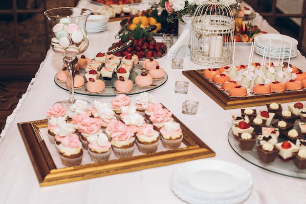 結婚披露宴のテーブルの上に花で飾られたおいしいキャンディスウィートカップケーキポップ キャンディーバー お祝いのイベントやシャワーのためのおいしいピンクのお菓子 豪華でスタイリッシュなケータリング