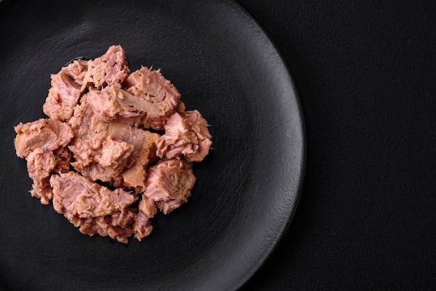 Foto deliziosa carne di tonno in scatola su un piatto di ceramica nera su uno sfondo di cemento scuro