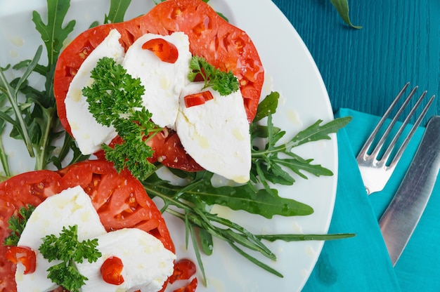 Delicious Caprese salad with mozzarella cheese, ripe tomatoes and fresh ruccola. Top view.