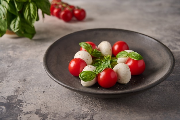 Delicious caprese salad with ripe tomatoes fresh basil and mozzarella cheese in black plate on the