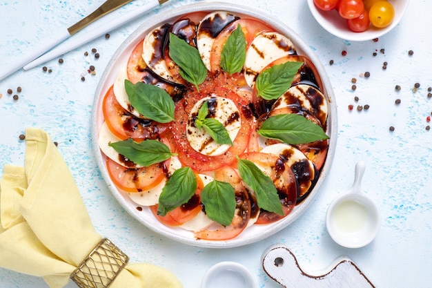 Deliziosa insalata caprese con pomodori maturi e mozzarella, foglie di basilico fresco, olio d'oliva e salsa balsamica. cibo italiano. vista dall'alto piatto laico su sfondo blu