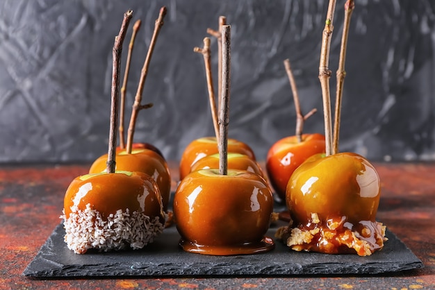 Delicious caramel apples with tree branches on slate plate