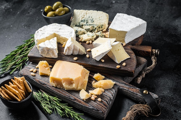 Delizioso tagliere di formaggi. assortimento di formaggi, camembert, brie, gorgonzola, parmigiano, olive, noci ed erbe aromatiche. sfondo nero. vista dall'alto.