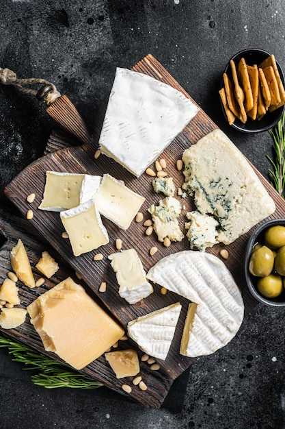 Delicious cheese board assortment of cheese camembert brie\
gorgonzola parmesan olives nuts and herbs black background top\
view