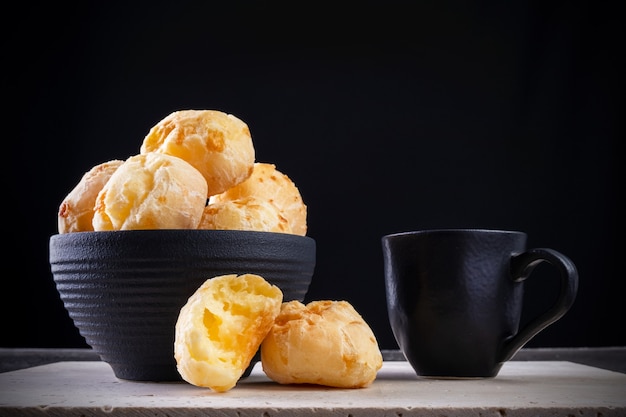 Delicious cheese breads and a cup of coffee on white marble with black background.