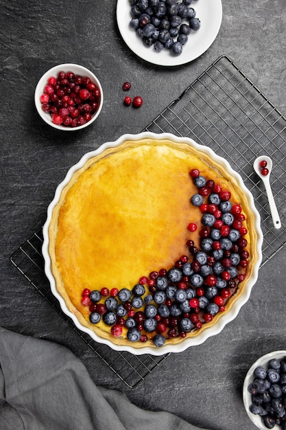 Delicious cheesecake tart with fresh blueberries and cranberries, on a dark stone.