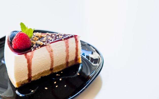 Delicious cheesecake with berries and mint on black ceramic plate over white backdrop