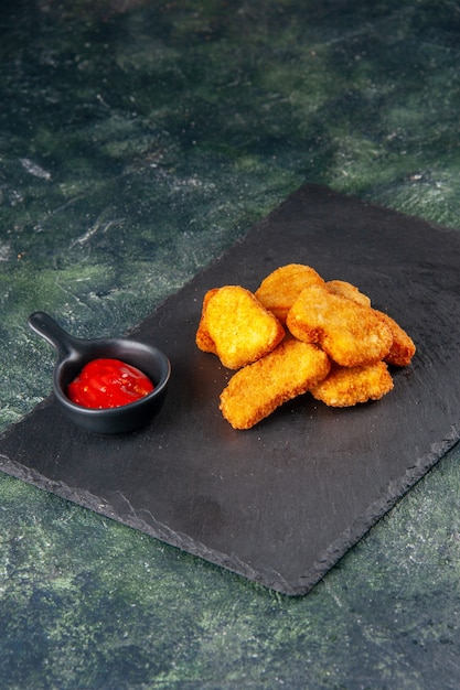 Delicious chicken nuggets and ketchup on black tray on dark color surface