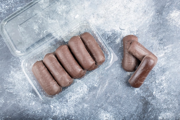 Delicious chocolate bar cakes in plastic container on marble surface