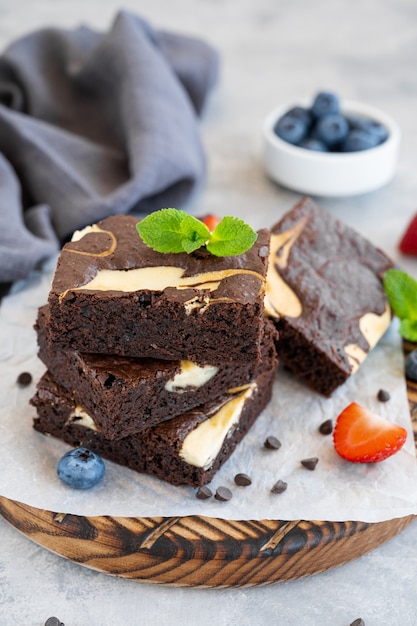 Delicious chocolate brownie cheesecake with fresh berries and mint on a wooden board