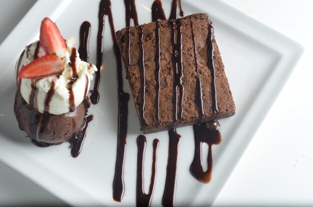 Foto un delizioso brownie al cioccolato servito con gelato su un piatto bianco isolato