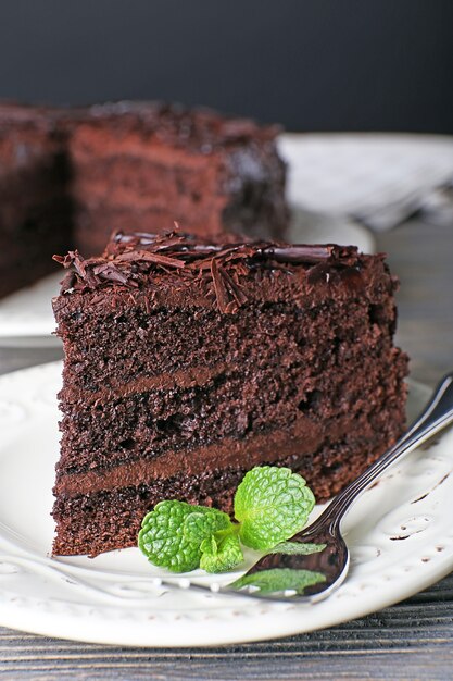 Delicious chocolate cake in white plate with mint on wooden table, closeup