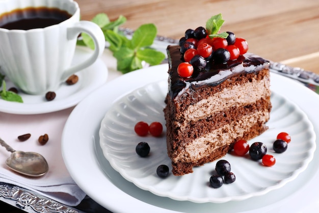 Delicious chocolate cake with berries and cup of coffee on table close up