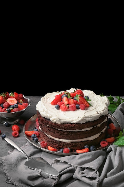 Delicious chocolate cake with berries on table against black background