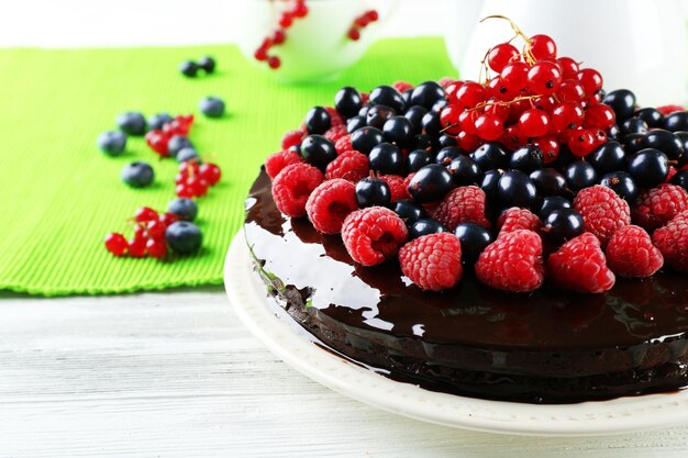 Delicious chocolate cake with summer berries on wooden table with green napkin closeup