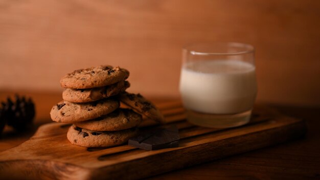 Delicious chocolate chip cookies with a glass of milk on a wooden board against wooden background