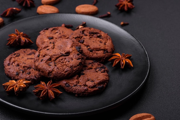 Вкусное шоколадное печенье с орехами на черной керамической тарелке на темном бетонном фоне