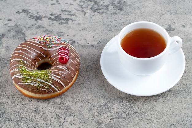 Вкусный шоколадный глазированный пончик и чашка чая на каменном фоне.