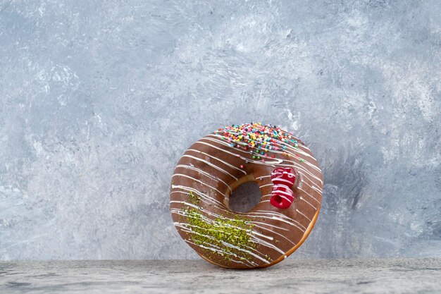 Delicious chocolate glazed donut with sprinkles on stone background. 