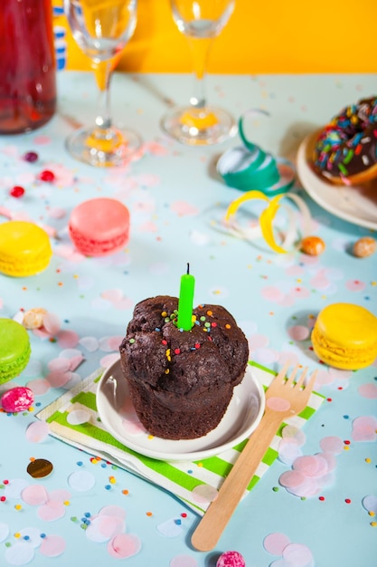 Вкусный шоколадный кекс с праздничной свечой и другими сладостями и конфетами на заднем плане. Концепция партии.