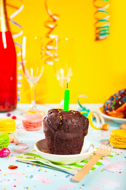 Delicious chocolate muffin cupcake with birthday candle and other sweets and candies on the background. party concept