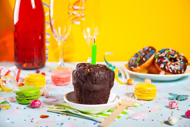 Delicious chocolate muffin cupcake with birthday candle and other sweets and candies on the background. party concept