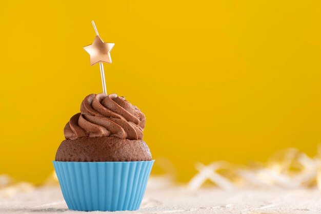 Delicious chocolate muffin with buttercream frosting with candles in the shape of star on yellow background.