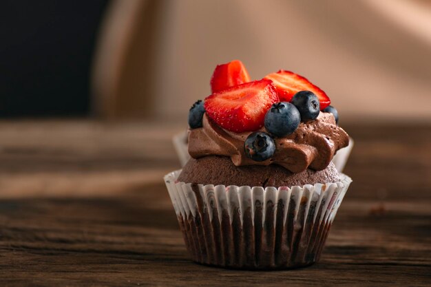 Delicious chocolate muffin with creamy glaze and fresh berries Cupcake with strawberries and blueberries close up