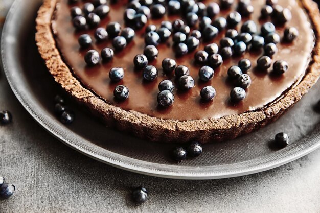 Delicious chocolate tart with blueberry on grey table closeup