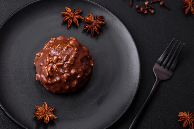 Delicious chocolate tart with nuts on a black ceramic plate on a dark concrete background