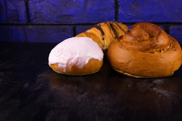 Delicious cinnamon rolls icing and chocolate croissant on a dark wooden background