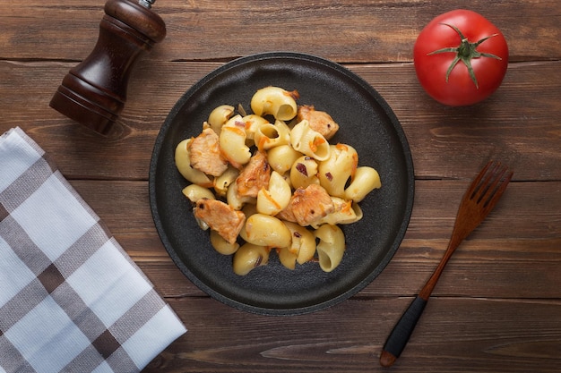 Photo delicious classic pasta with chicken pieces and fried vegetables on a plate on a wooden table