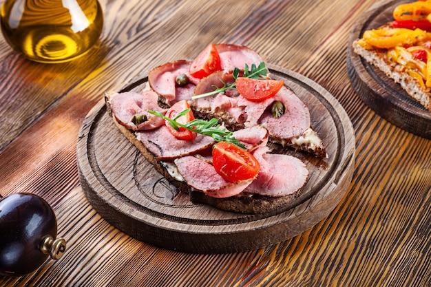 Vista deliziosa del primo piano sulla bruschetta con arrosto di manzo sul tagliere. pane tostato fresco italiano su fondo di legno con lo spazio della copia libera per progettazione. cucina italiana per menu o ricetta. spuntino sano