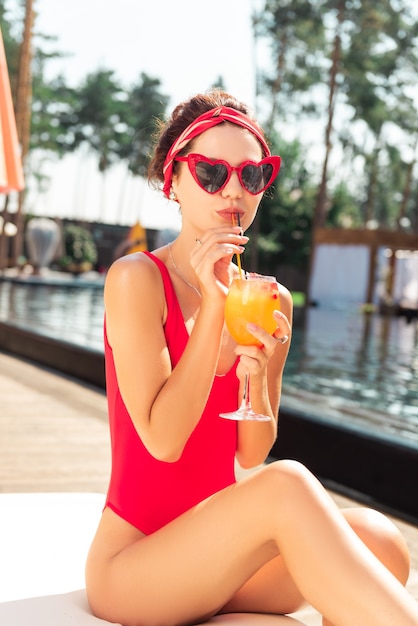 Delicious cocktail. Attractive fashionable woman holding a straw while drinking a cocktail