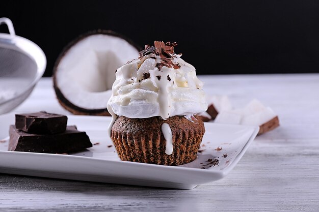 Delicious coconut cupcake with cream and chocolate chips on color wooden table and dark background