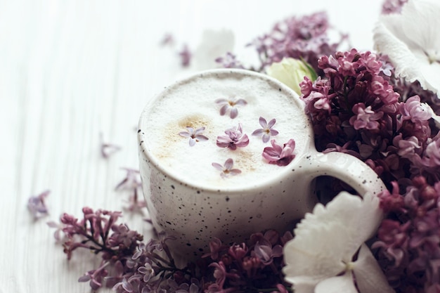 Delicious coffee with lilac petals rose and lilac branch on white wood Good morning still life