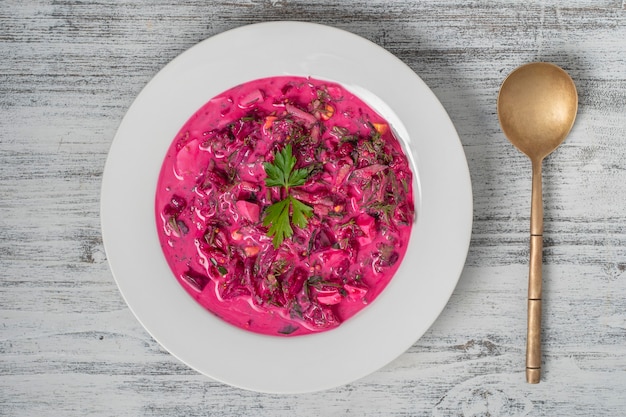 Delicious cold summer beetroot soup with cucumber, boiled egg, radish in white plate on table, close up, top view