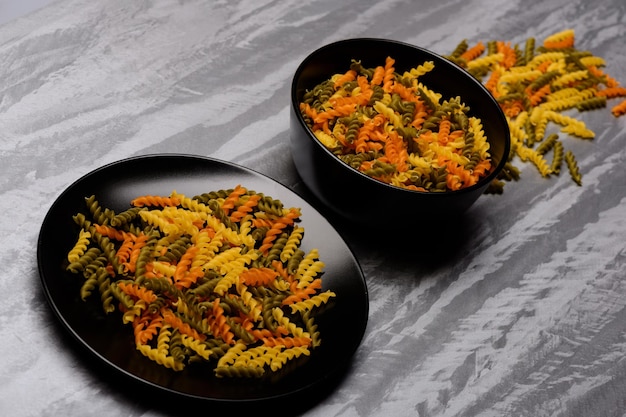 Delicious colorful Italian pasta in two black ceramic plates on grey textured background side view