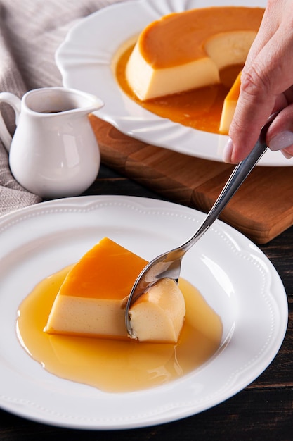 Delicious condensed milk pudding on white plate Someone scooping up a piece with a spoon